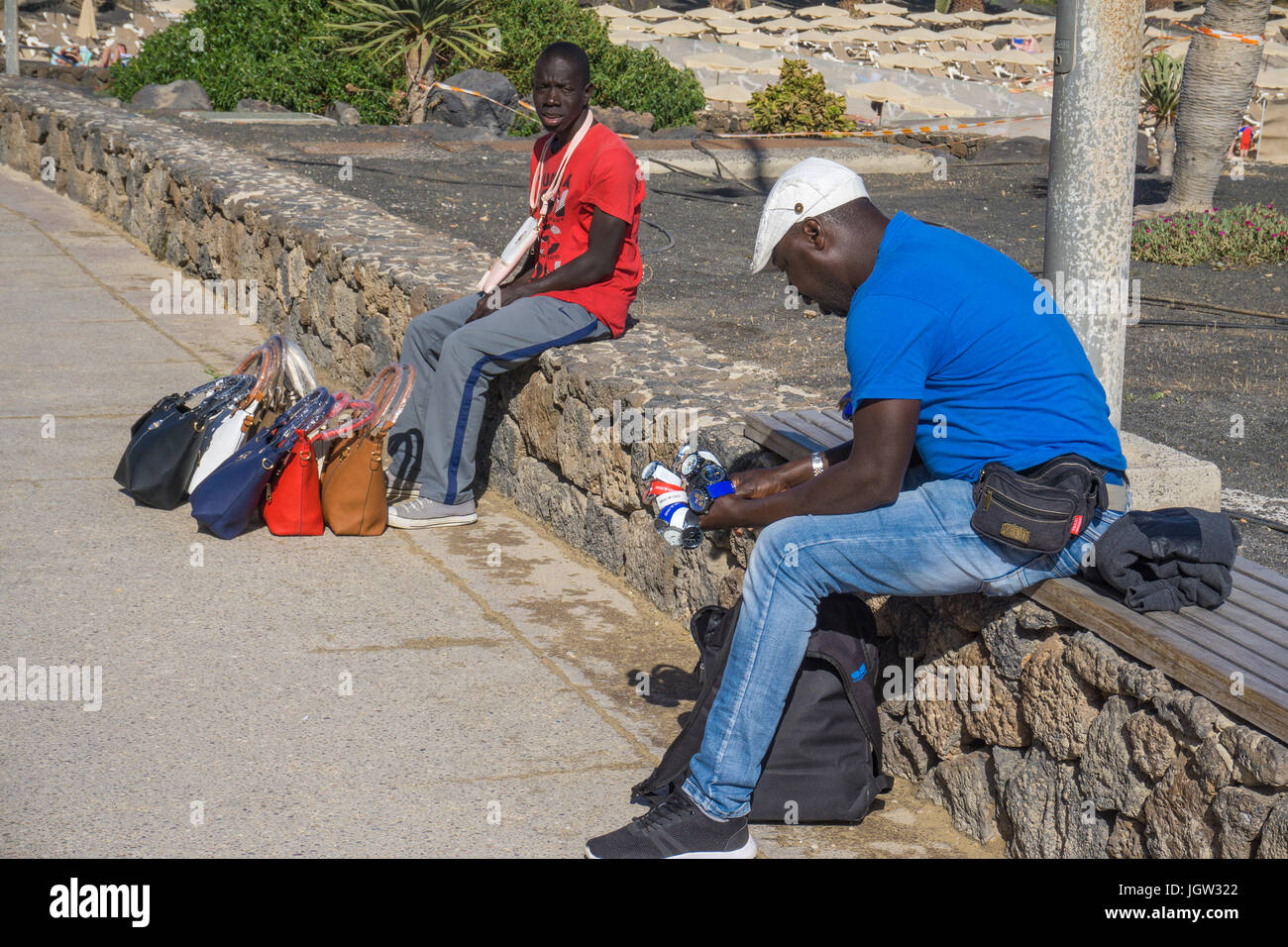Afrikanische Straße Verkäufer versuchen, Handtaschen und Uhren zu Strandpromenade Playa de las Cucharas, Costa Teguise, Lanzarote, Kanarische Inseln, Europa zu verkaufen Stockfoto