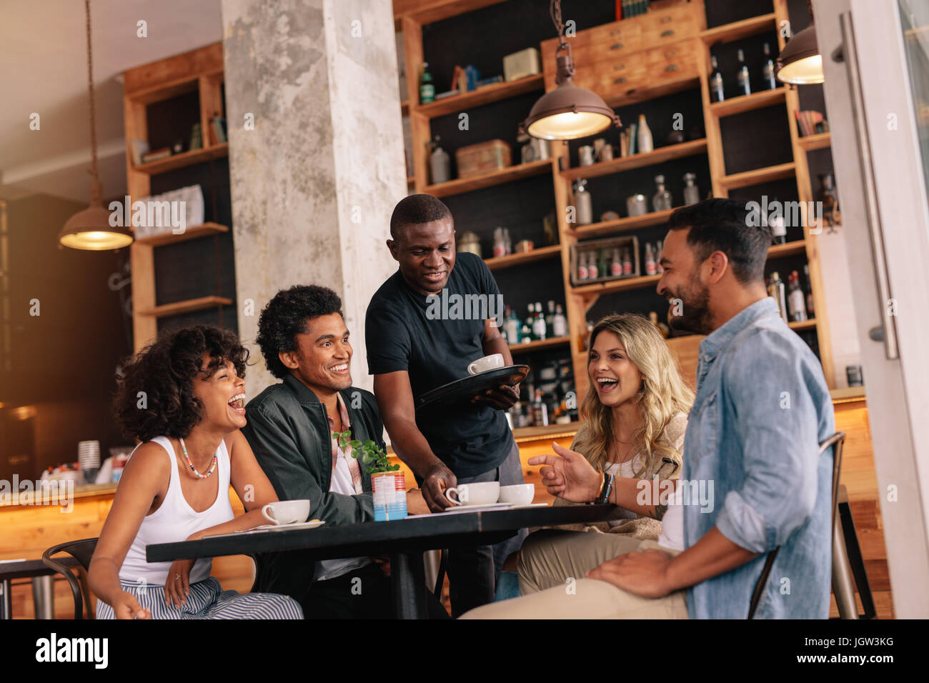 Gruppe von Freunden sitzen um den Tisch und Kellner serviert Kaffee im Café. Die Jugendlichen treffen im Café. Stockfoto