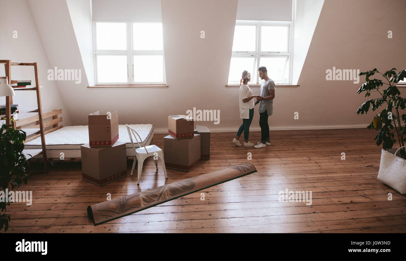 Junges Paar in der Liebe eine neue Wohnung einziehen. Mann und Frau stehen zusammen mit Boxen und Teppich am Boden. Stockfoto