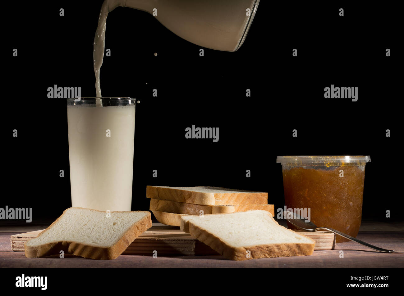 Portion Milch mit Scheiben Brot und Marmelade auf dem Tisch auf schwarzem Hintergrund Stockfoto