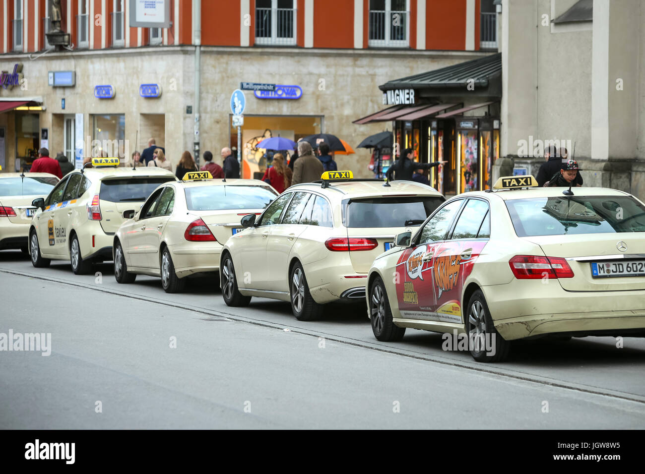 München, Deutschland - 9. Mai 2017: Passanten auf der Straße neben dem aufgereiht geparkten Taxis in München. Stockfoto