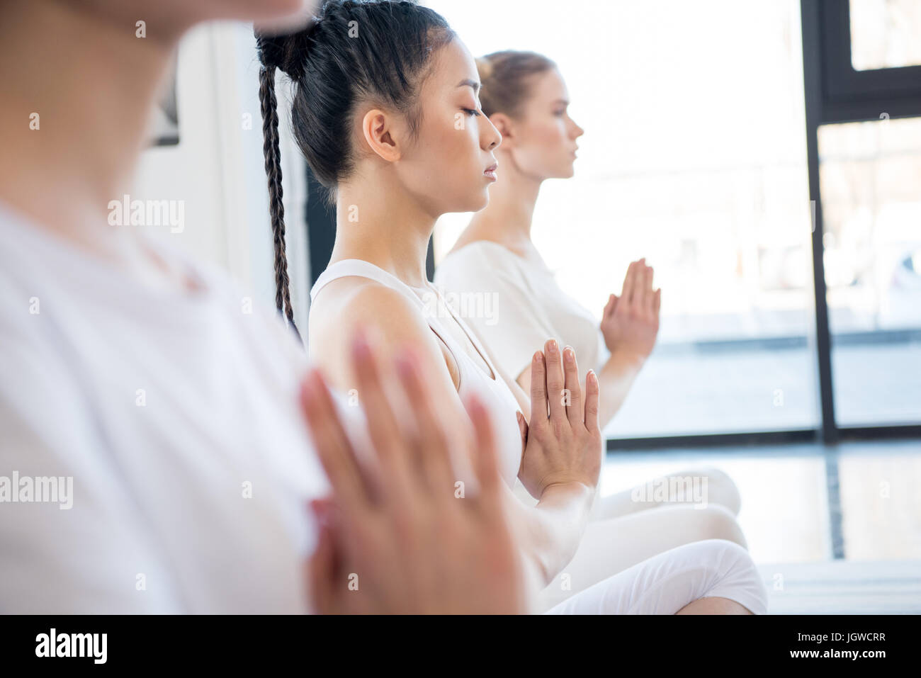 Junge Frauen meditieren im Lotus Pose mit Namaste Mudra-Geste im Innenbereich konzentriert Stockfoto