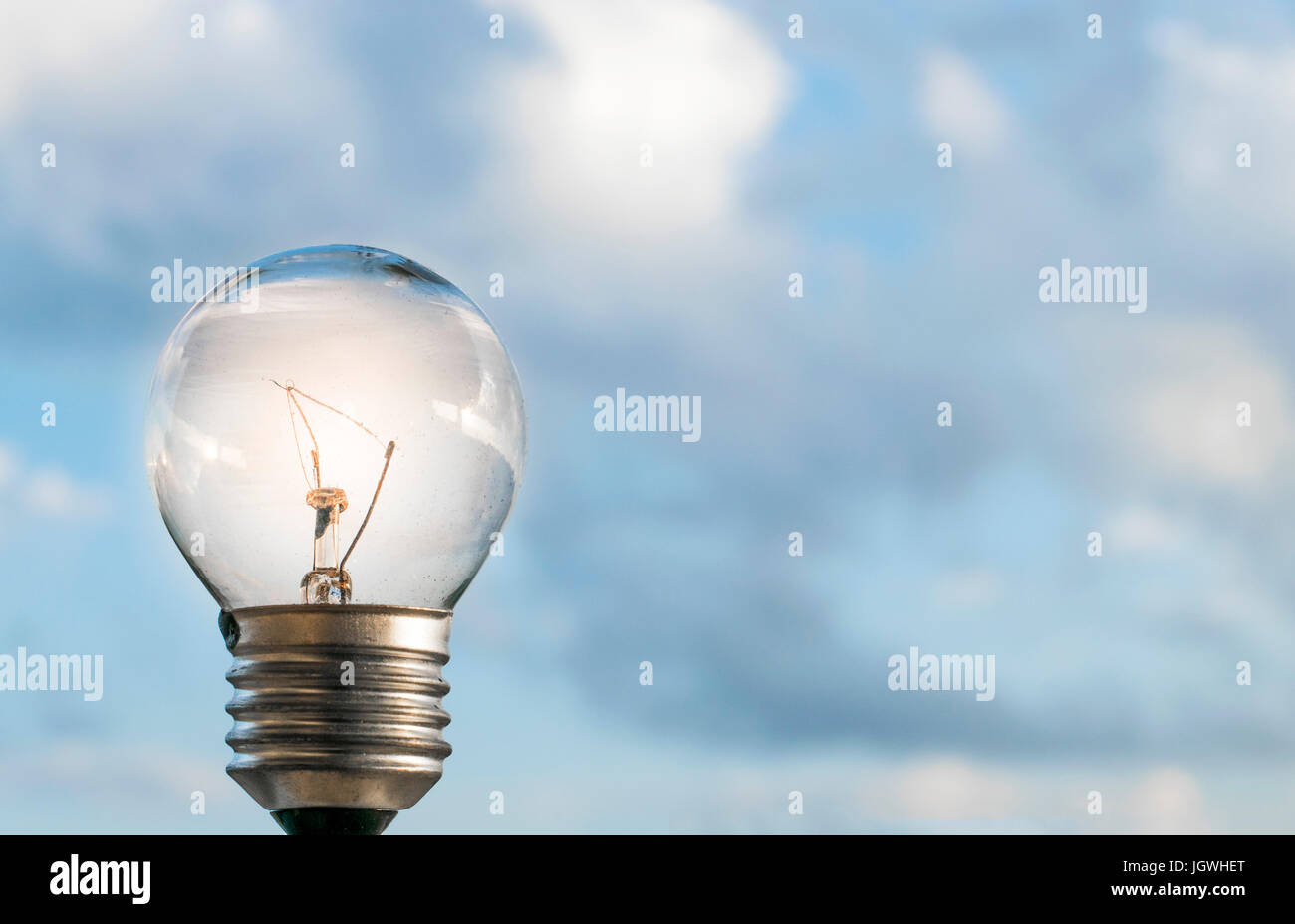 Beleuchteten Glühbirne Lampe mit dem blauen Himmel außerhalb und Wolken im Hintergrund Stockfoto