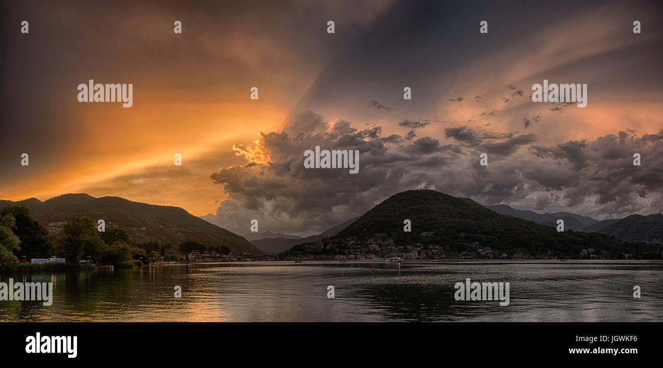 Sonnenuntergang über den Luganer See in ein Ende des den Sommertag mit bewölktem Himmel und sonnigen Lichtstrahl Stockfoto