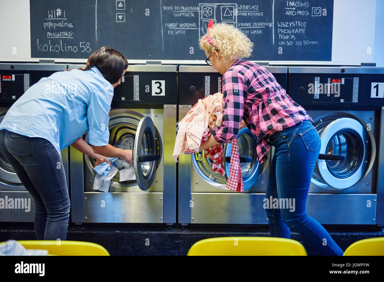 Zwei Frauen, die Waschmaschinen im Waschsalon Wäsche einlegen Stockfoto