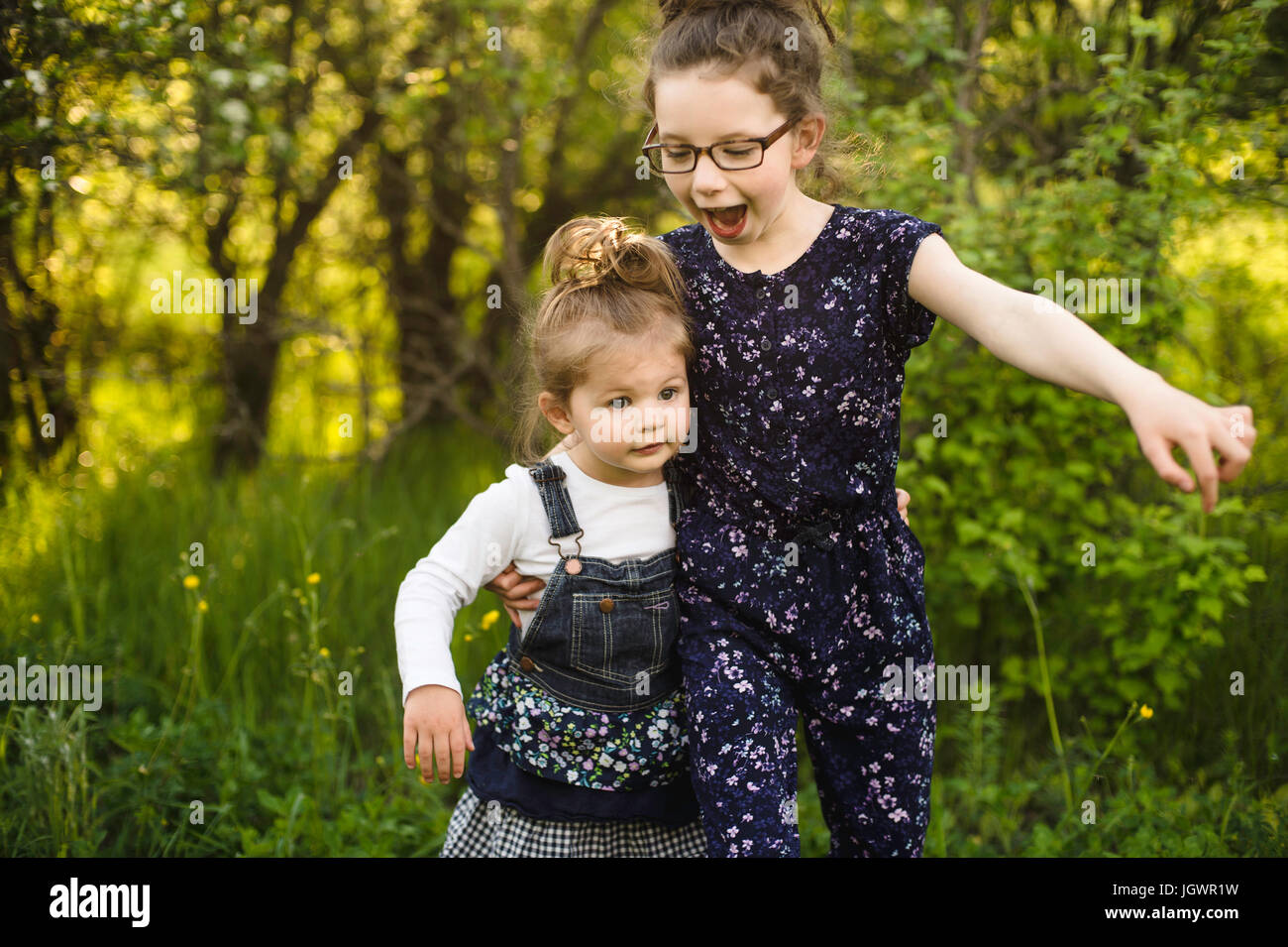 Mädchen und kleine Schwester spielen im Feld mit Bäumen Stockfoto