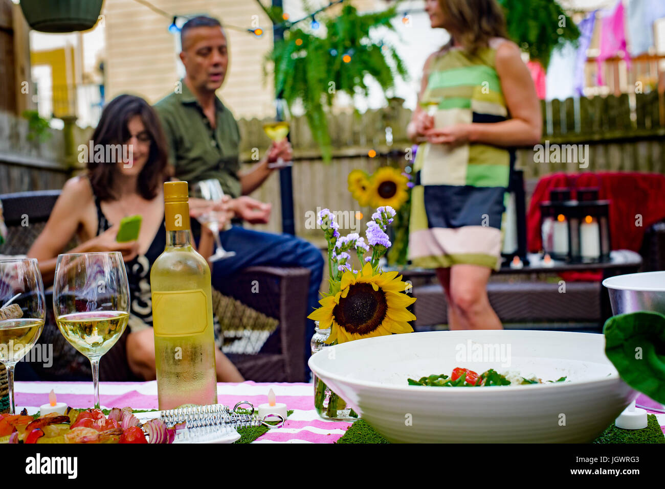 Gruppe von Menschen auf Gartenparty, hält Gläser Wein, Flasche Wein und Essen auf Servierplatten im Vordergrund Stockfoto