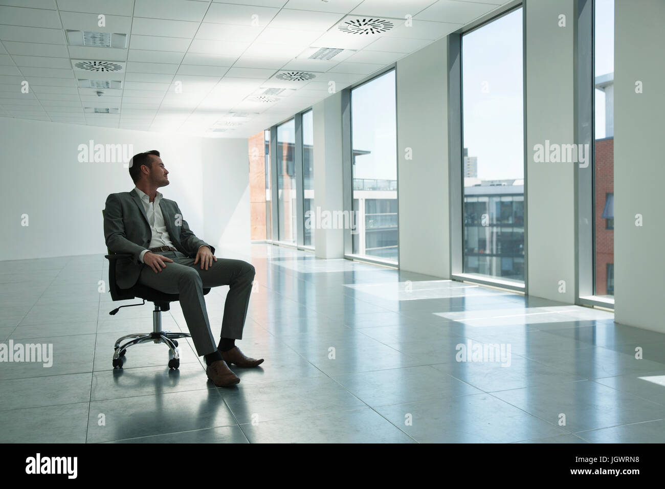 Geschäftsmann, sitzen im Stuhl in leeren Büroflächen, Blick aus Fenster Stockfoto