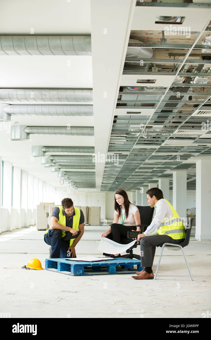 Drei Leute sitzen in neu errichteten Büroflächen, Baupläne zu betrachten Stockfoto