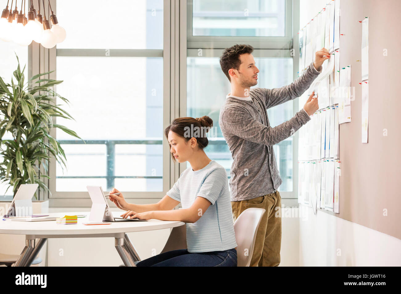 Weibliche digital Designer schreiben auf Laptop und Kollegen arrangieren Moodboard im Büro Stockfoto