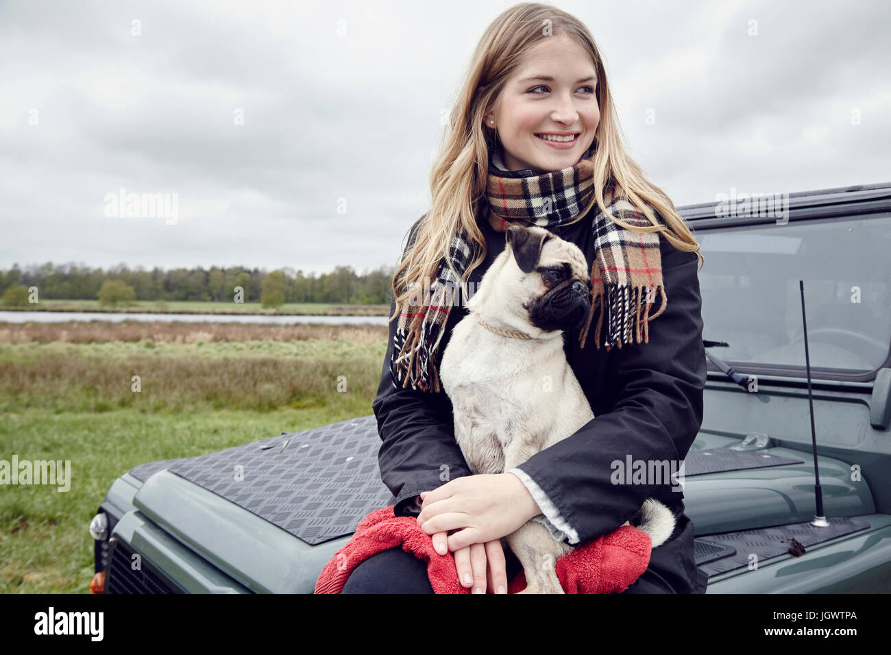 Junge Frau sitzt auf Geländewagen im Feld mit Hund auf Schoß Stockfoto