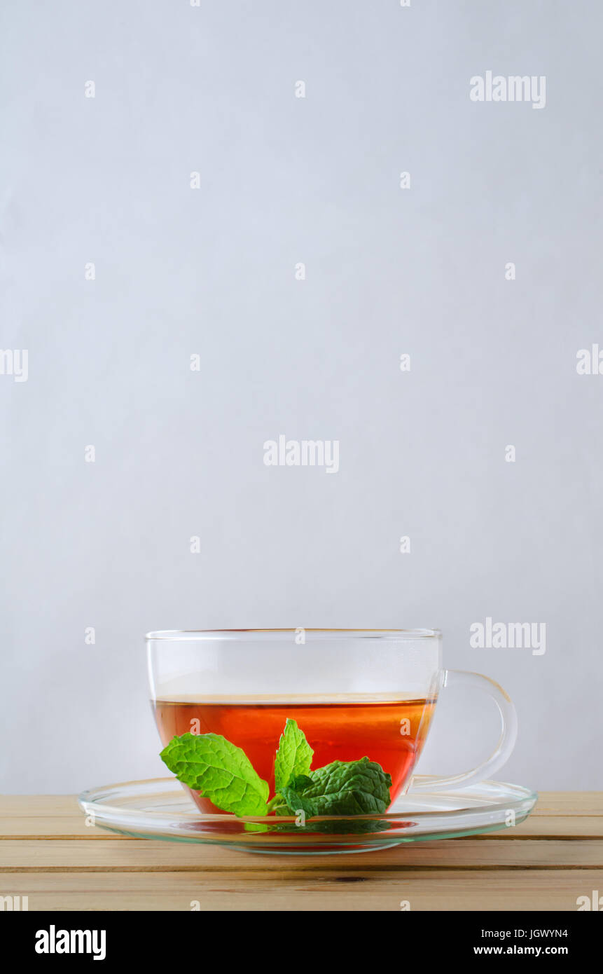 Vertikale Aufnahme einer Glas-Tasse mit Tee mit einem Stück Zitrone auf einem Holztisch.  Ein Zweig Minze beruht auf der Untertasse.  Kopieren Sie Raum über. Stockfoto