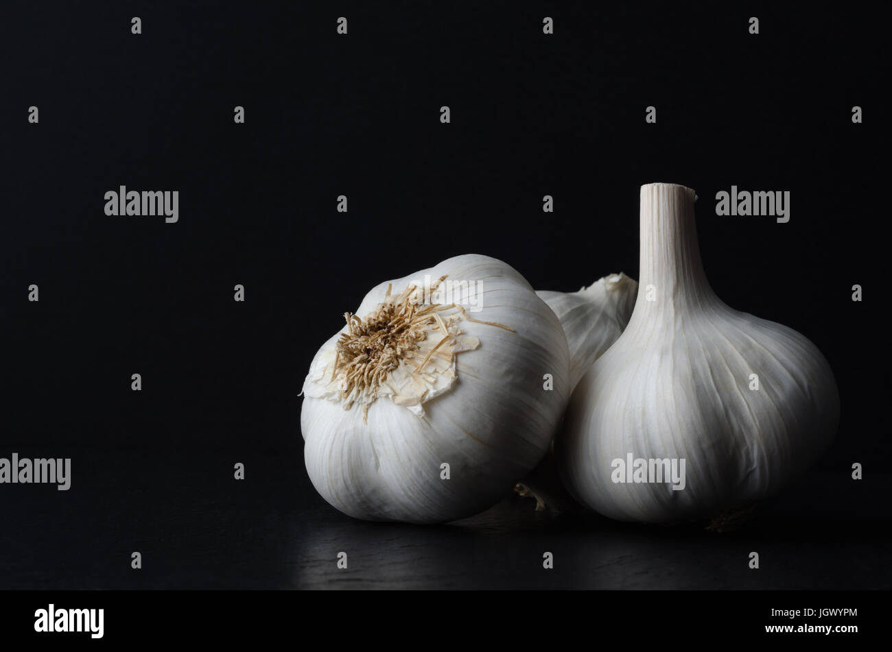 Stillleben-Zusammensetzung der drei ganze Knoblauch Zwiebeln auf schwarzem Schiefer auf schwarzem Hintergrund. Stockfoto