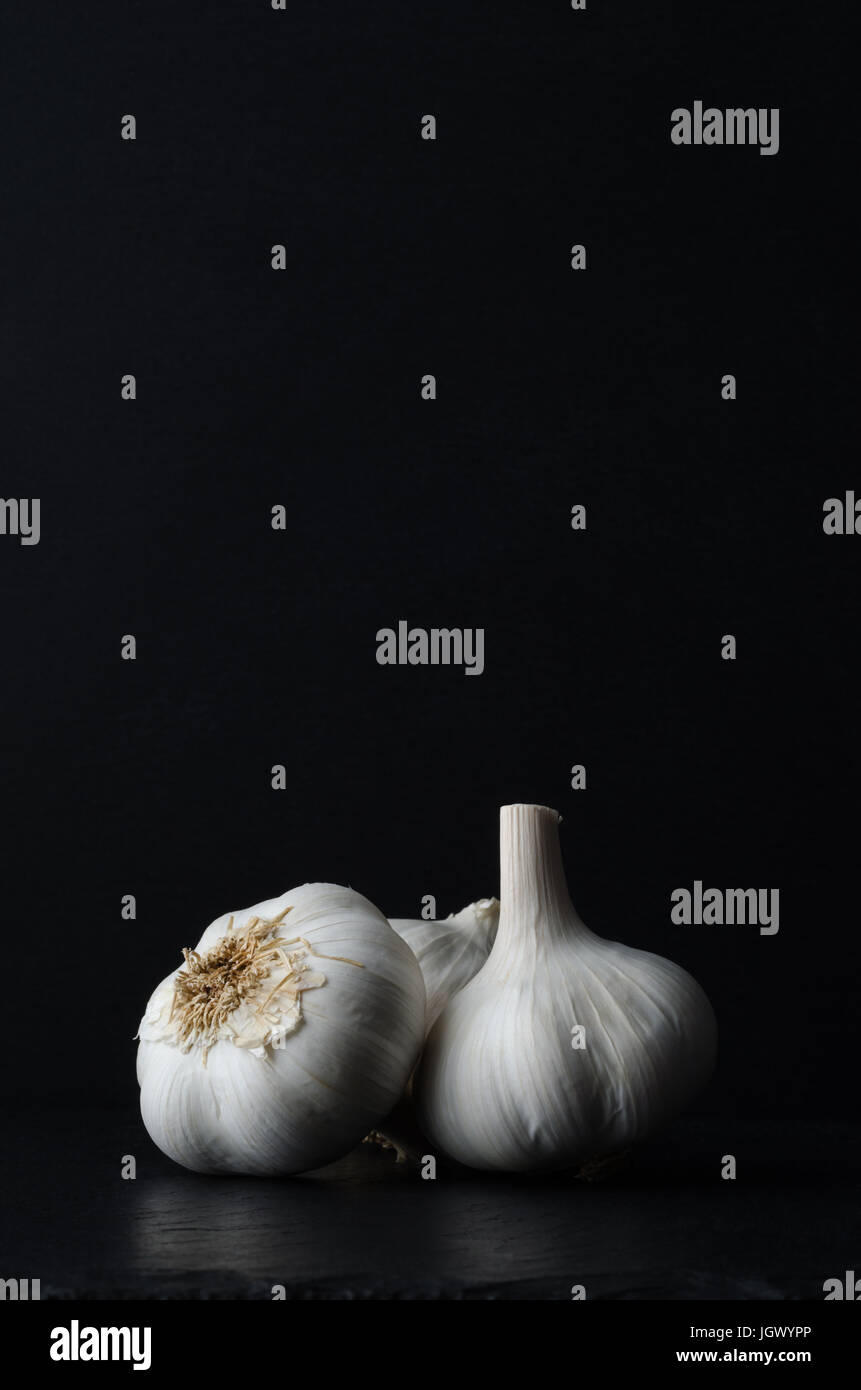 Stillleben-Zusammensetzung der drei ganze Knoblauch Zwiebeln auf schwarzem Schiefer auf schwarzem Hintergrund. Stockfoto