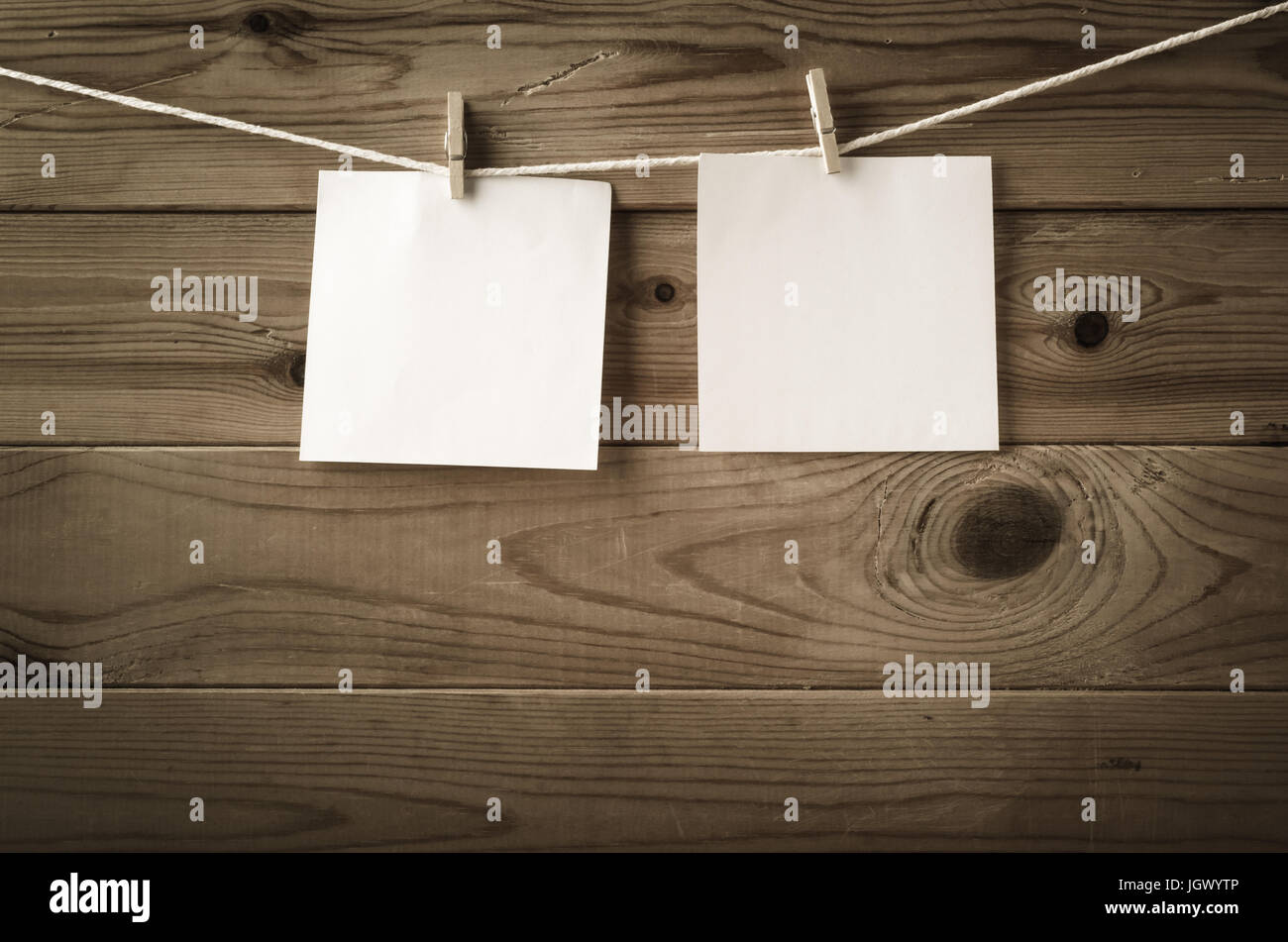 Zwei Quadrate von leeres Papier, gekoppelt an eine Zeichenfolge, die Wäscheleine mit Holzbrett Zaun im Hintergrund.  Niedrige Sättigung und Vignette gibt ein Retro oder vi Stockfoto