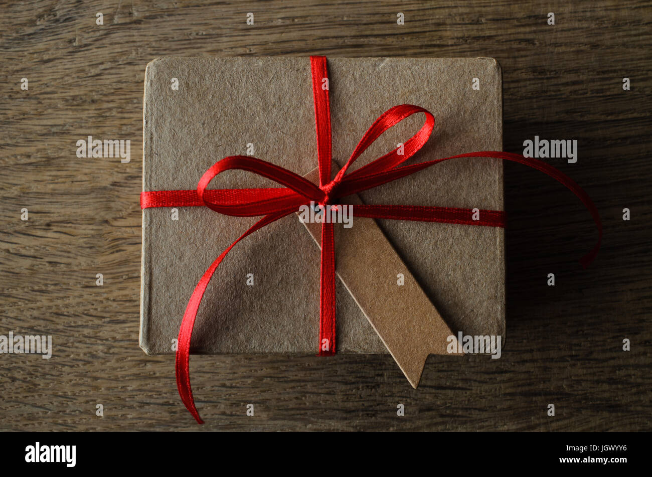 Schlichte braune Karton Geschenk-Box mit leeren Vintage-Stil eingekerbt Geschenkanhänger, auf einem Bogen mit dünnen roten Satinband gebunden.  Overhead Schüsse aufs Holz Eichentisch Stockfoto