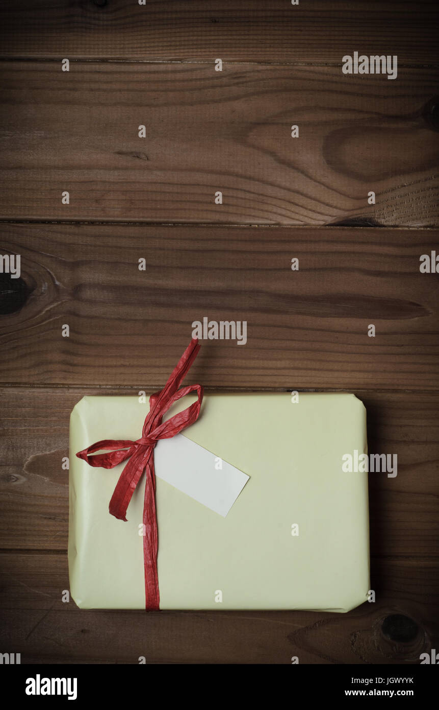 Aufwand für ein Geschenk-Paket in hellgelb gewickelt und gebunden um mit roter Bast Band auf geplankte Holzoberfläche zu beugen.  Farben angepasst und vignette hinzugefügt fo Stockfoto