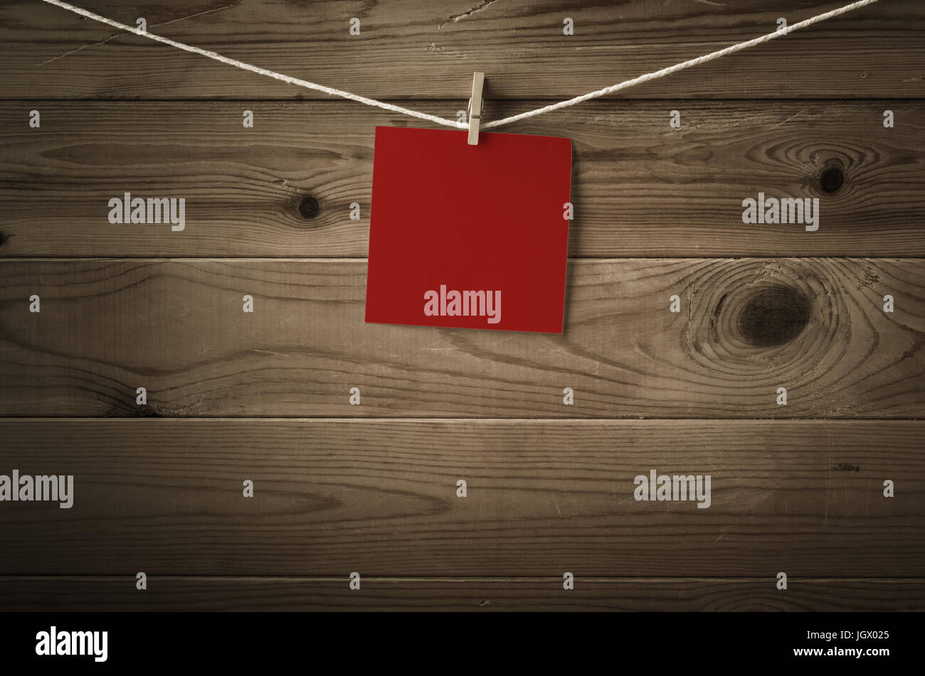 Eine einzelne Quadrat der festlichen roten Notizpapier, gekoppelt an eine Zeichenfolge, die Wäscheleine.  Holzbohle Hintergrund.  Niedrige Sättigung und Vignette gibt eine Retro-o Stockfoto