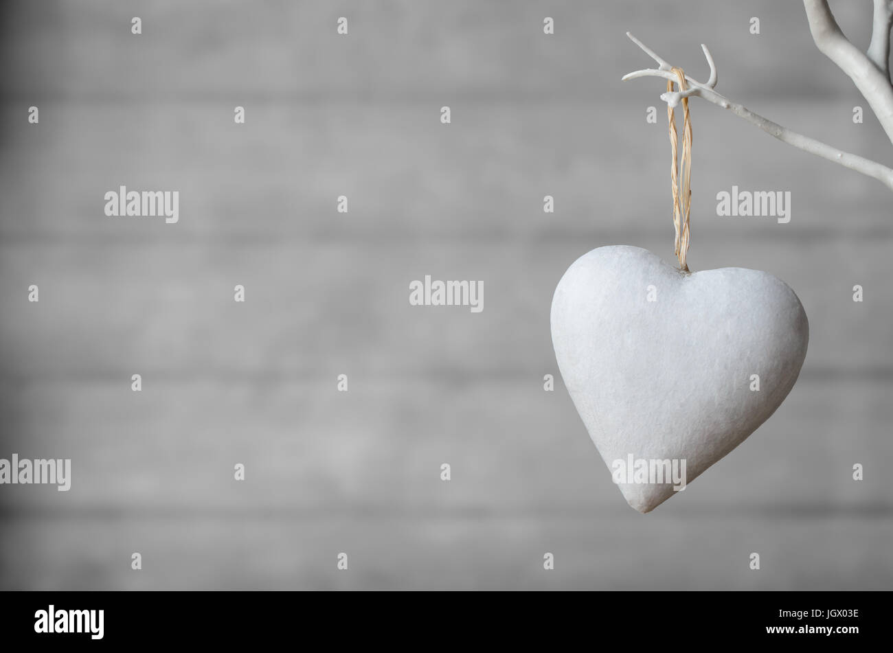 Ein weiß lackierter Herz, von weißen künstlichen Baum mit neutralen Holzbohle Weichzeichner Hintergrund hängen. Stockfoto