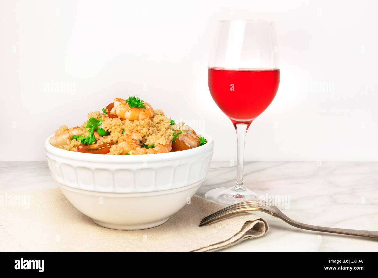 Ein Foto von einem Garnelen-Couscous mit Cherry-Tomaten, Petersilie und grüne Erbsen mit einem Glas Rosé und ein Platz für text Stockfoto