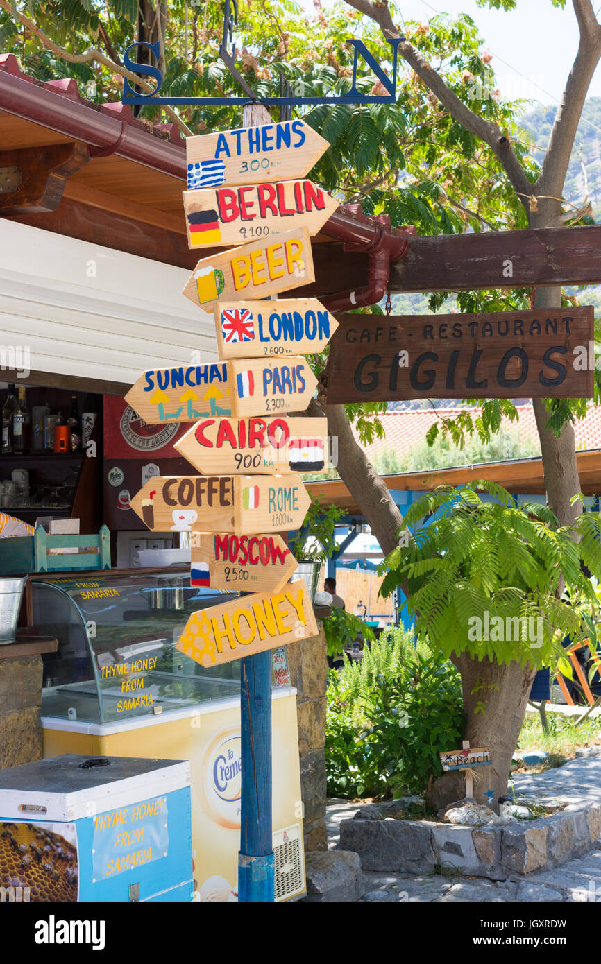 Colouful Richtung Wegweiser vor einem Restaurant auf Kreta mit Entfernungen zu einigen der weltweit wichtigsten Städten und zu den lokalen Bier, Kaffee und Honig-Verkaufsstelle Stockfoto