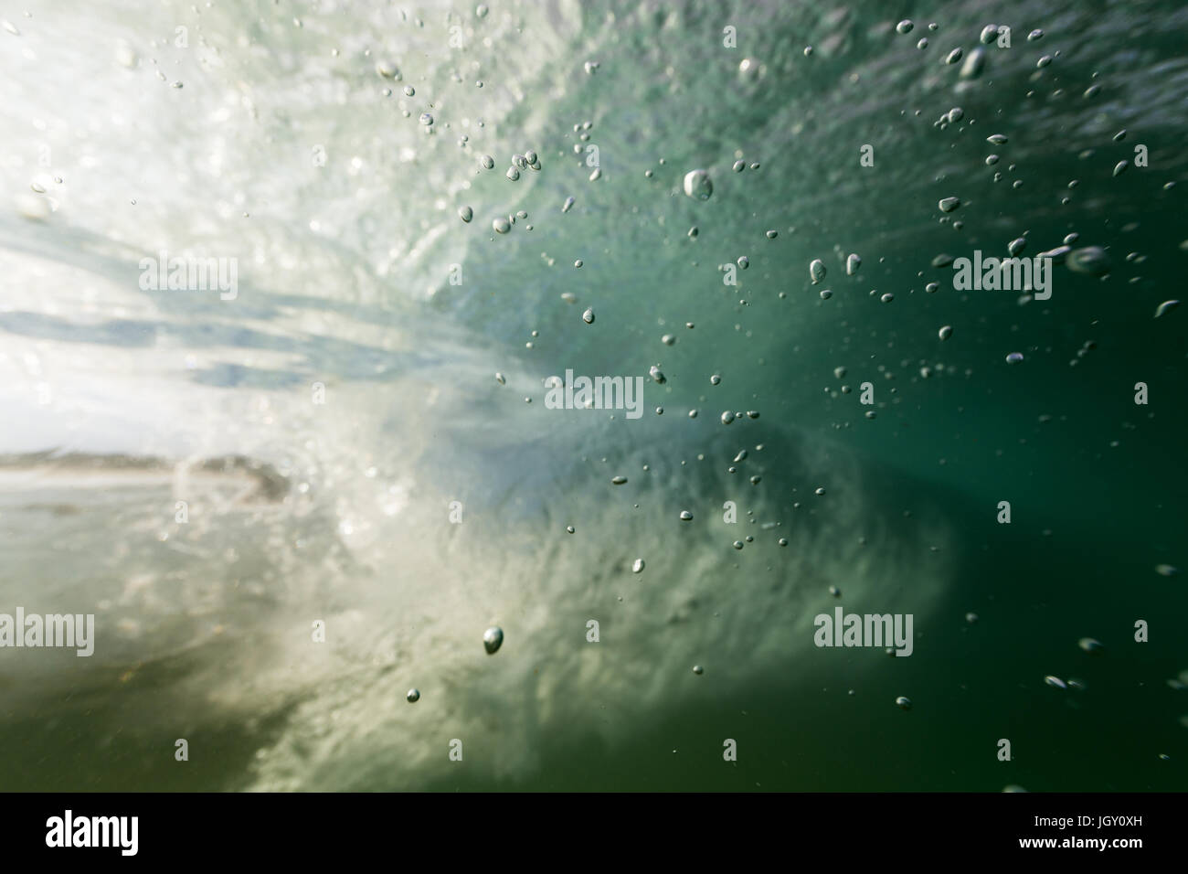 Luftblasen steigen in klaren Meerwasser aus dem Meeresboden in dieser Unterwasser Aufnahme wie eine brechende Welle geht in den Hintergrund. Stockfoto