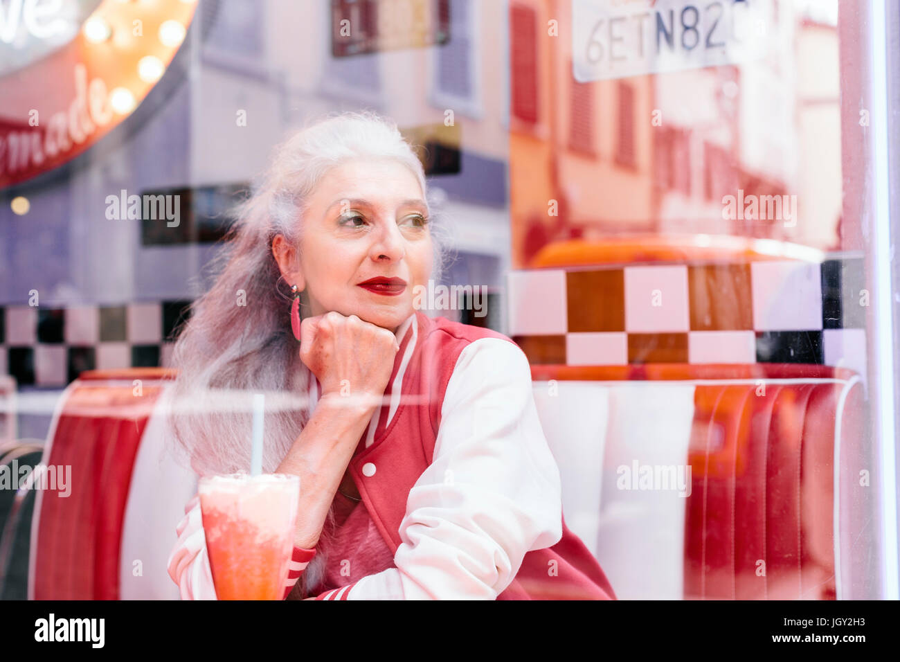 Reife Frau in Baseballjacke Blick durch Fenster aus 50er Jahre diner Stockfoto