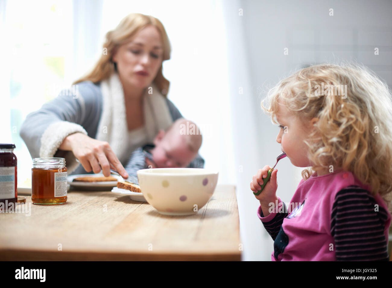 Mutter hält Baby Boy, mit kleinen Tochter am Küchentisch sitzen, frühstücken Stockfoto
