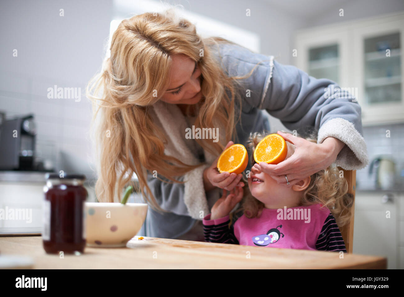 Junges Mädchen saß am Küchentisch, Mutter mit halbierten Orange vor Augen der Tochter Stockfoto