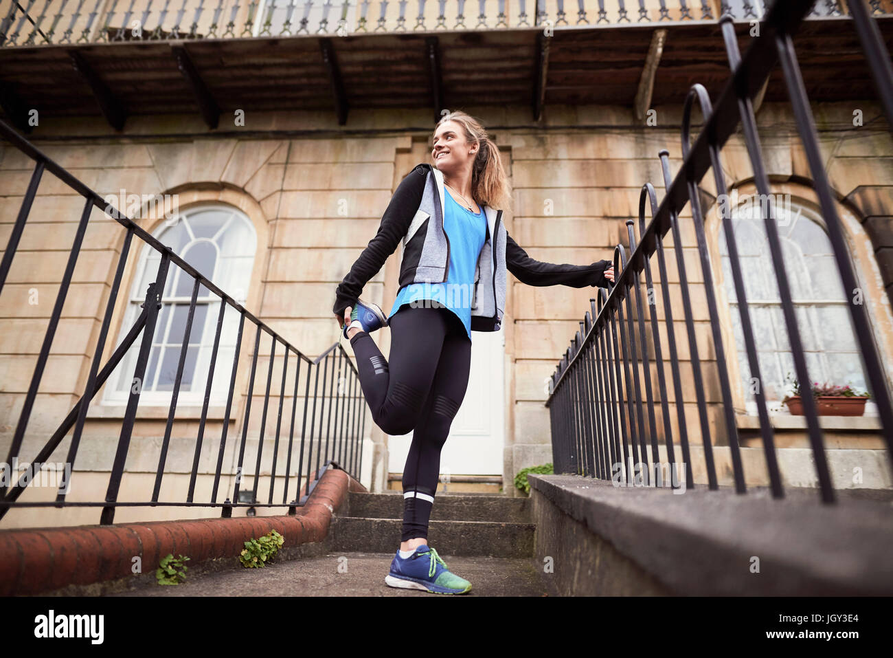Junge weibliche Läufer vor Haustür Dehnung Bein Stockfoto