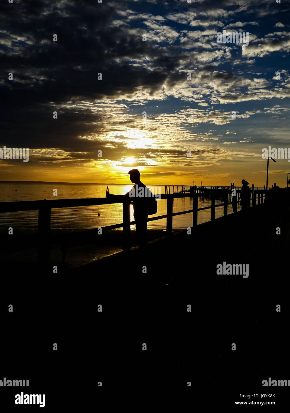 Silhouette eines Mannes stehend auf einem Steg hält eine Trinkflasche bei Sonnenuntergang auf Fraser Island, Queensland, Australien. Stockfoto