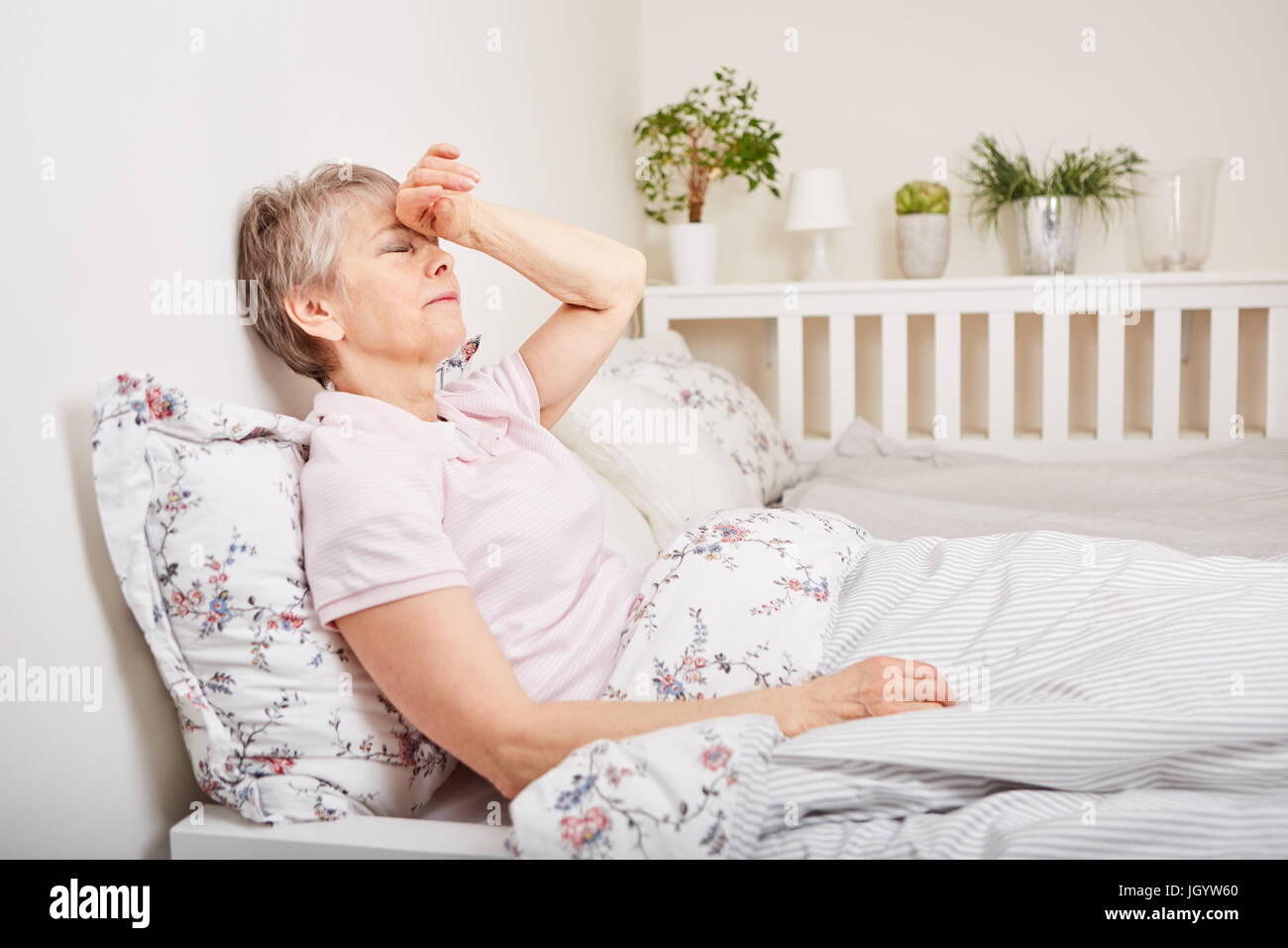 Ältere Frau mit der Krankheit liegen auf Bett mit Kopfschmerzen Stockfoto