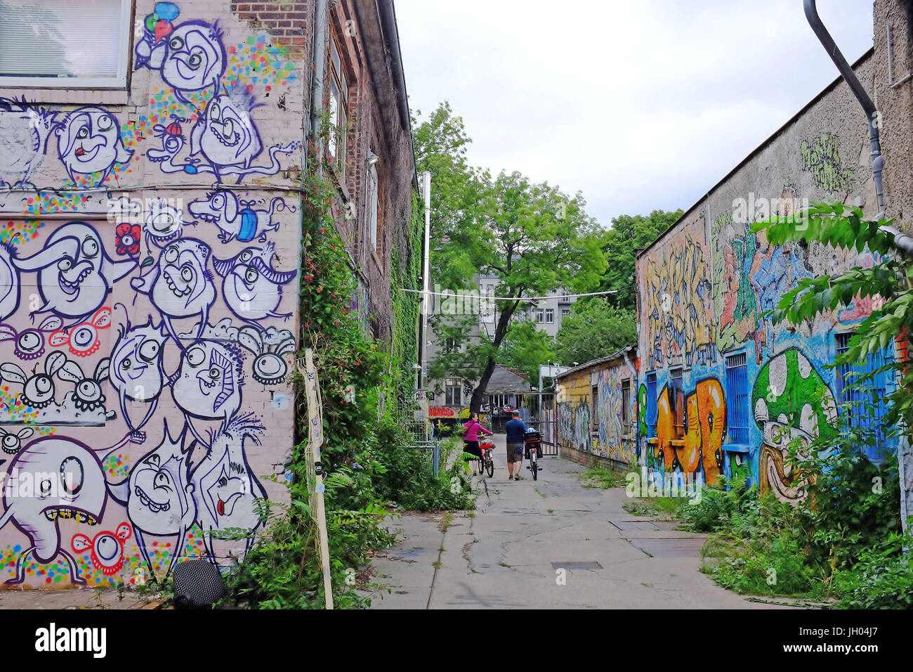 Zwei Menschen gehn ihre Räder durch eine Gasse, gefüllt mit street Art/Graffiti im Bereich Friedrichshain, Berlin, Deutschland Stockfoto