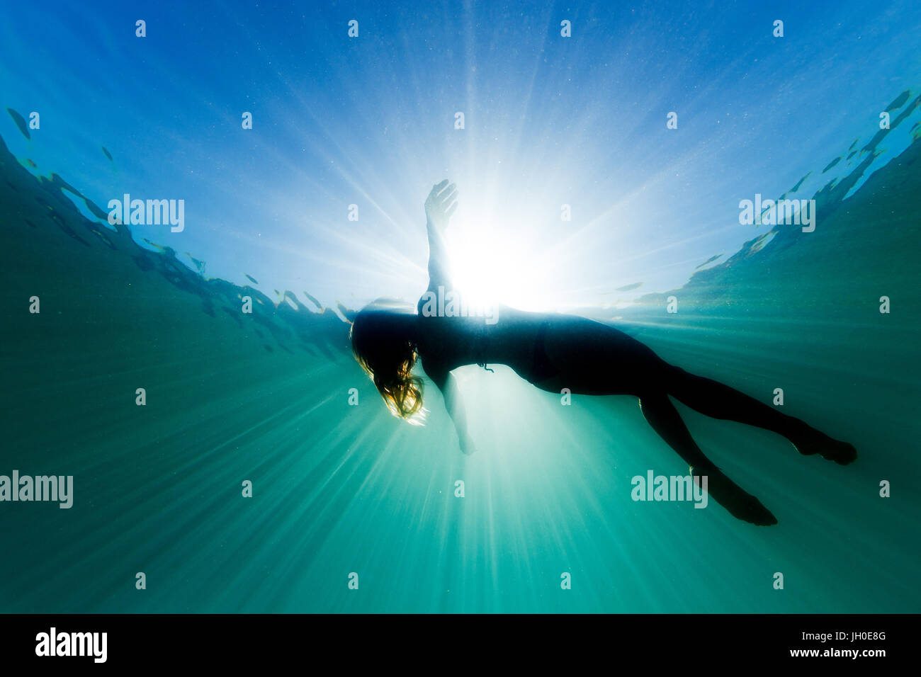 Eine schöne Frau schwimmt auf ihr zurück in den Ozean da sie umgeben ist, werden helle ätherische Licht und Sonne Strahlen. Stockfoto