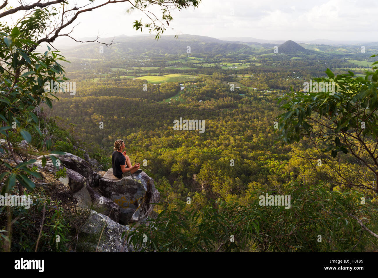 Ein junger Mann sitzt, ruhig auf einem Berg mit Weitblick in der Nähe von Noosa Heads, Australien zu meditieren. Stockfoto