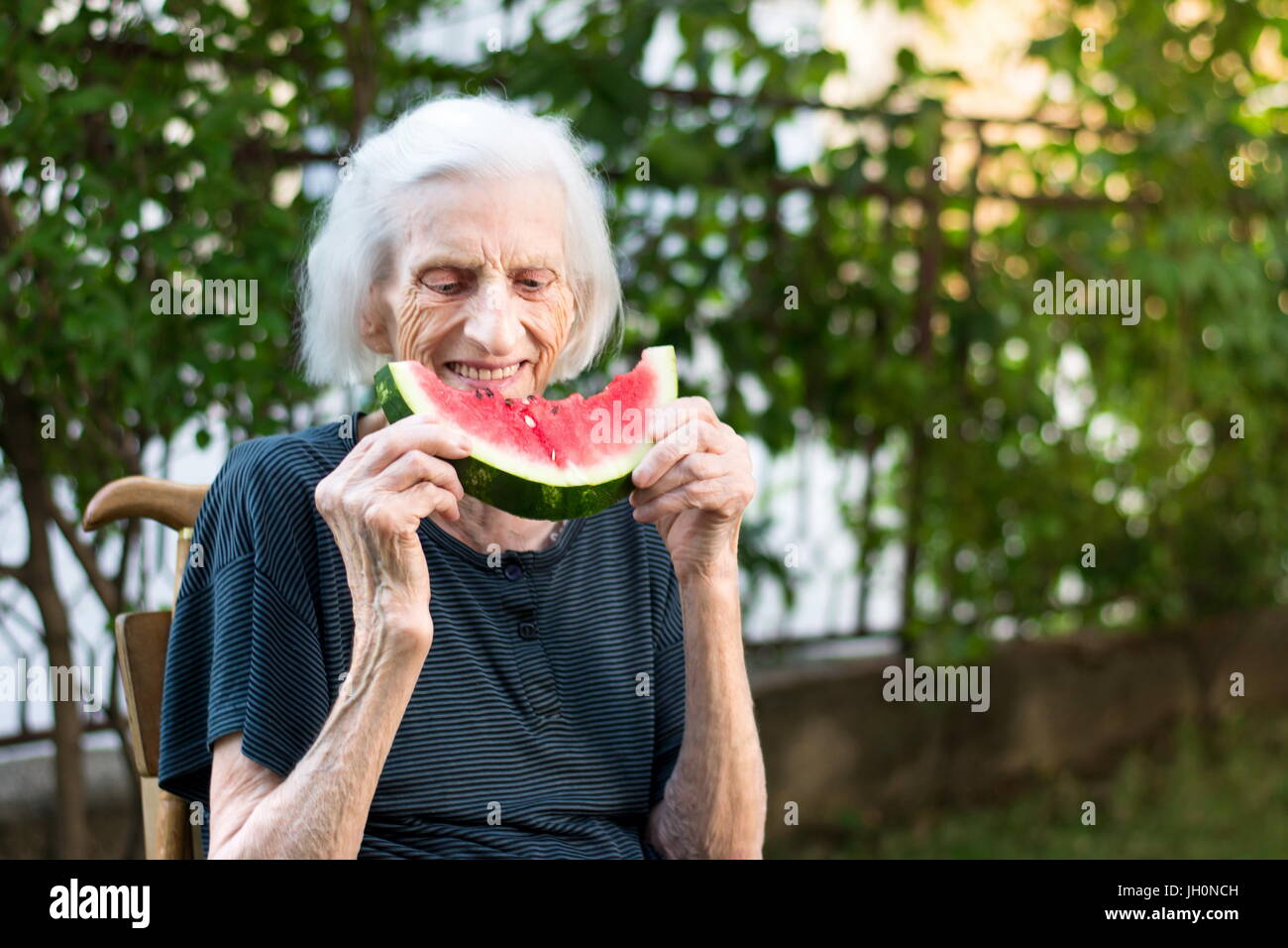 Fröhliche Oma Essen Wassermelone Frucht im Hinterhof Stockfoto