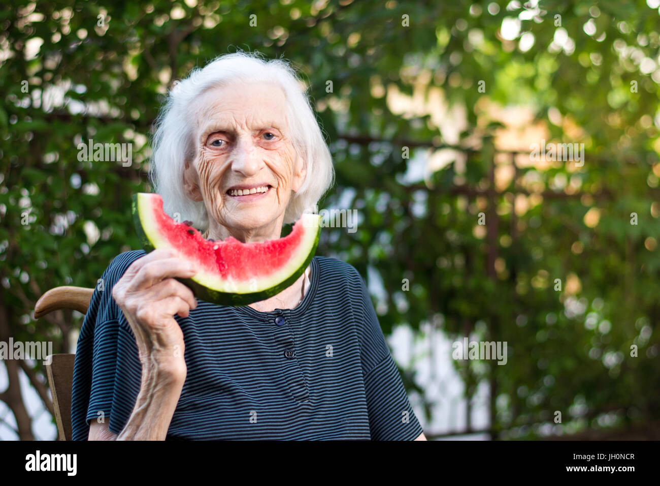 Fröhliche senior Frau hält Wassermelone Slice im Hinterhof Stockfoto