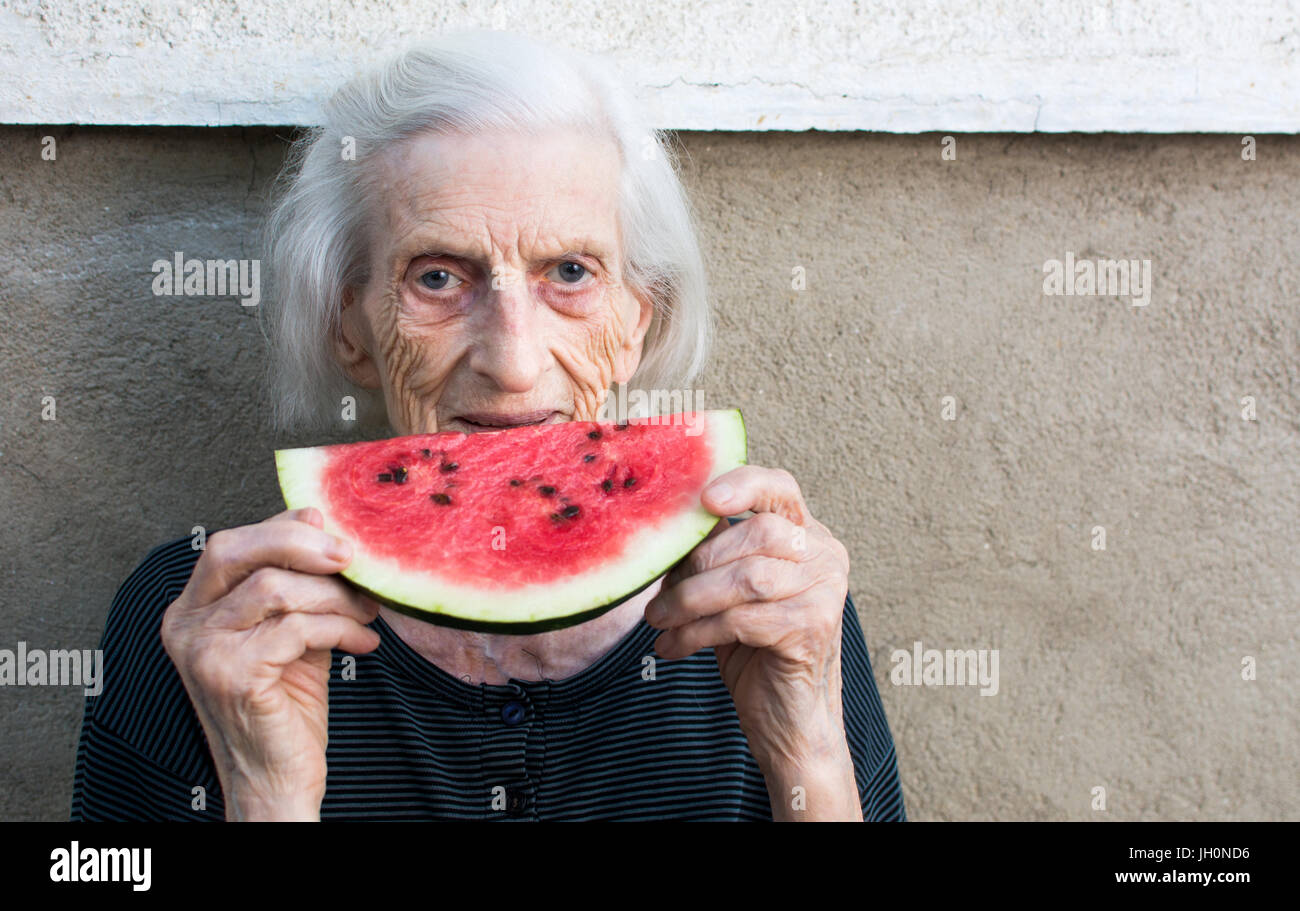 Fröhliche Oma Essen Wassermelone Frucht im Hinterhof Stockfoto