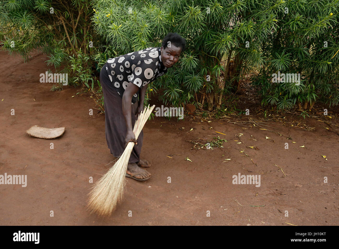 Frau die Erde rund um ihr Haus zu fegen. Uganda. Stockfoto