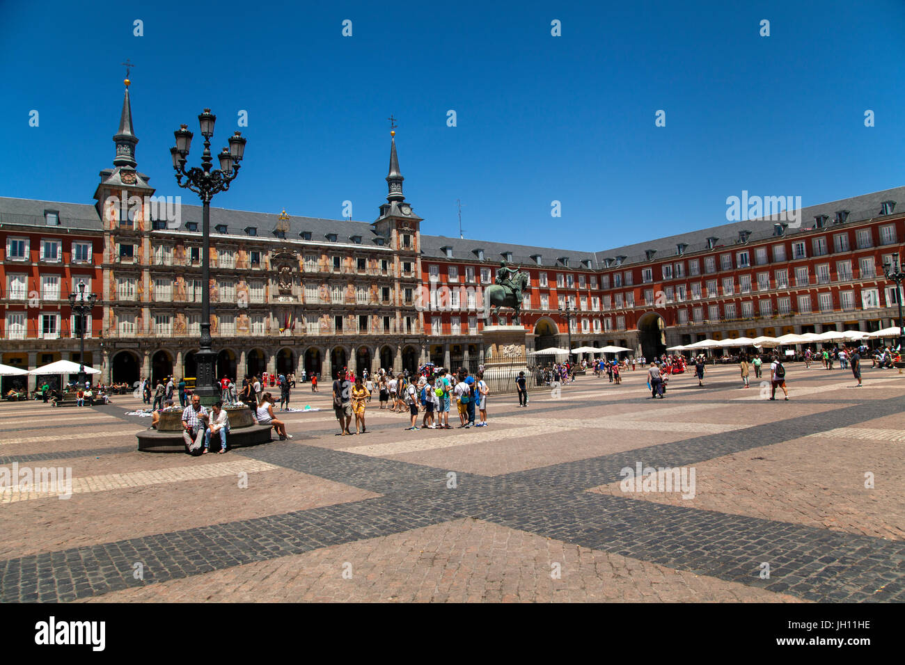 Touristen und Urlauber zu Fuß in der Plaza Mayor Madrid unter strahlend blauem Himmel Stockfoto