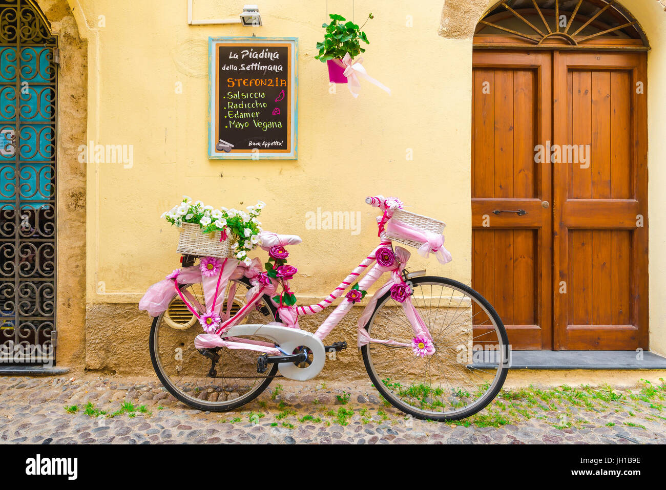 Fahrrad-Mittelmeer, lehnt eine bunt dekorierte Fahrrad gegen eine Wand bunt Restaurant in der Altstadt von Alghero, Nord-Sardinien. Stockfoto