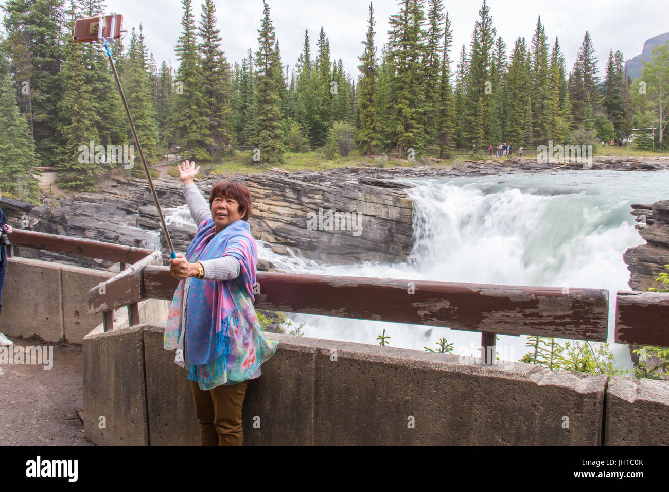 Eine Frau ist posiert und nehmen ein Selbstporträt mit einem Selfie-Stick an den Anthabasca Falls, Jasper Nationalpark, Alberta, Kanada Stockfoto