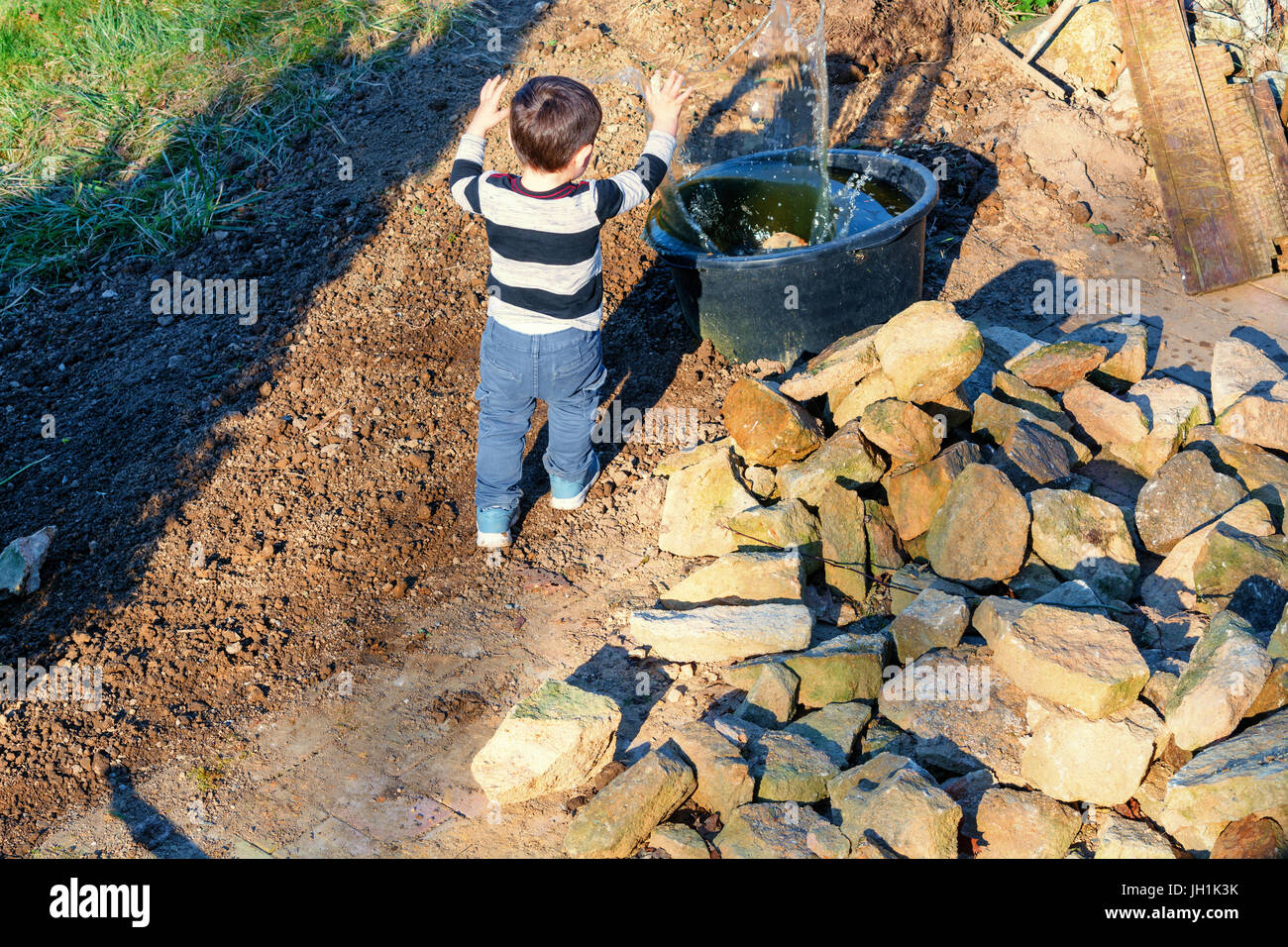 Kleiner Junge werfen einen Stein in ein Wasserfass Stockfoto
