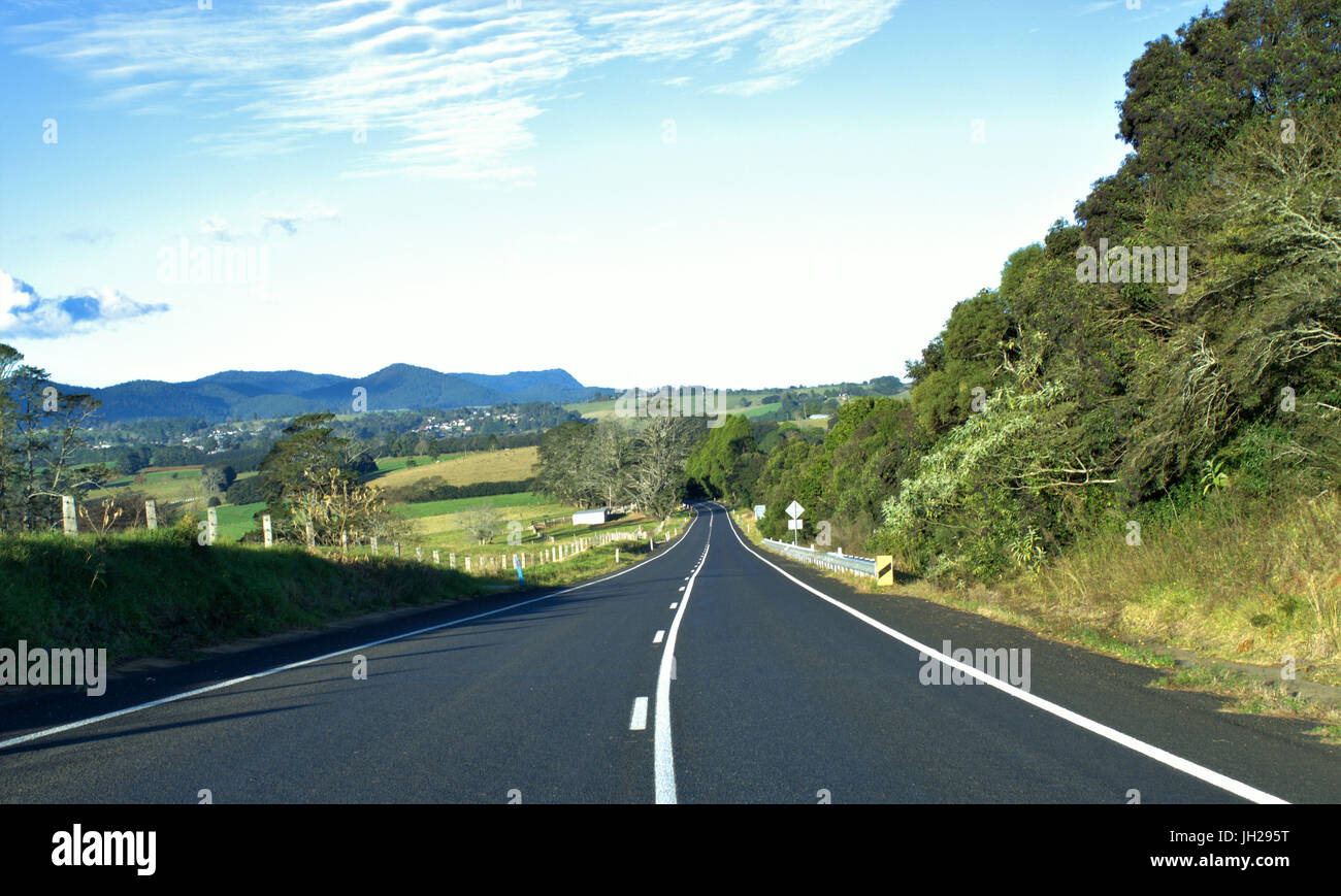 Schöne Landstraße mit grünem Rasen, Bäumen und blauen Himmel und Berge oben im Hintergrund in New South Wales Australien Stockfoto