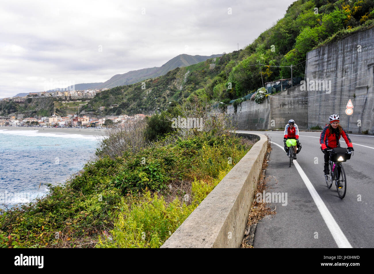 Zwei Radfahrer reiten ihre Fahrräder auf einer Küstenstraße in Kalabrien, Italien. Stockfoto