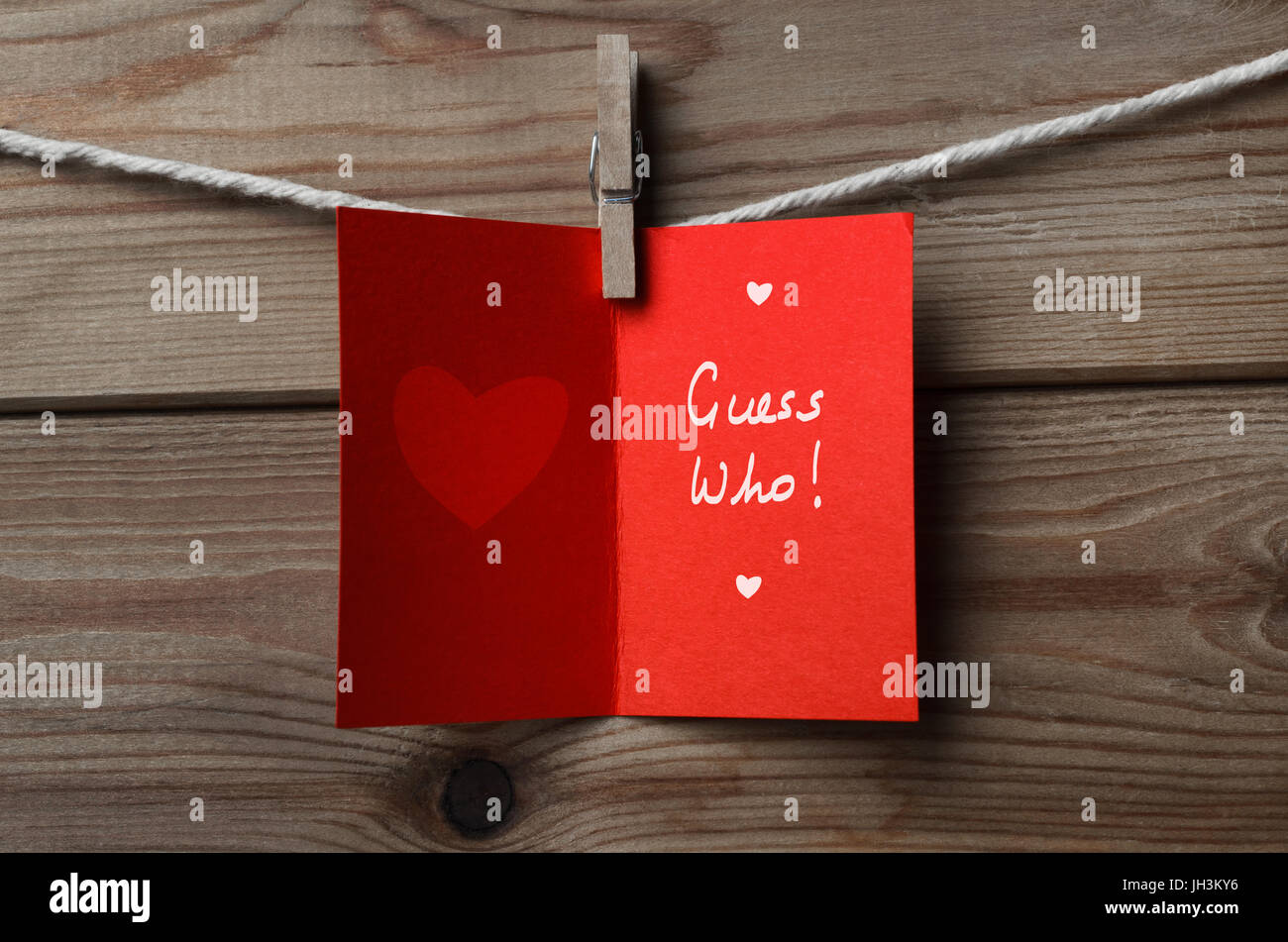 Eine geöffnete, rot Valentinstag Karte gekoppelt an Zeichenfolge Holzbohle Hintergrund mit den Worten "Guess Who" innen geschrieben. Stockfoto