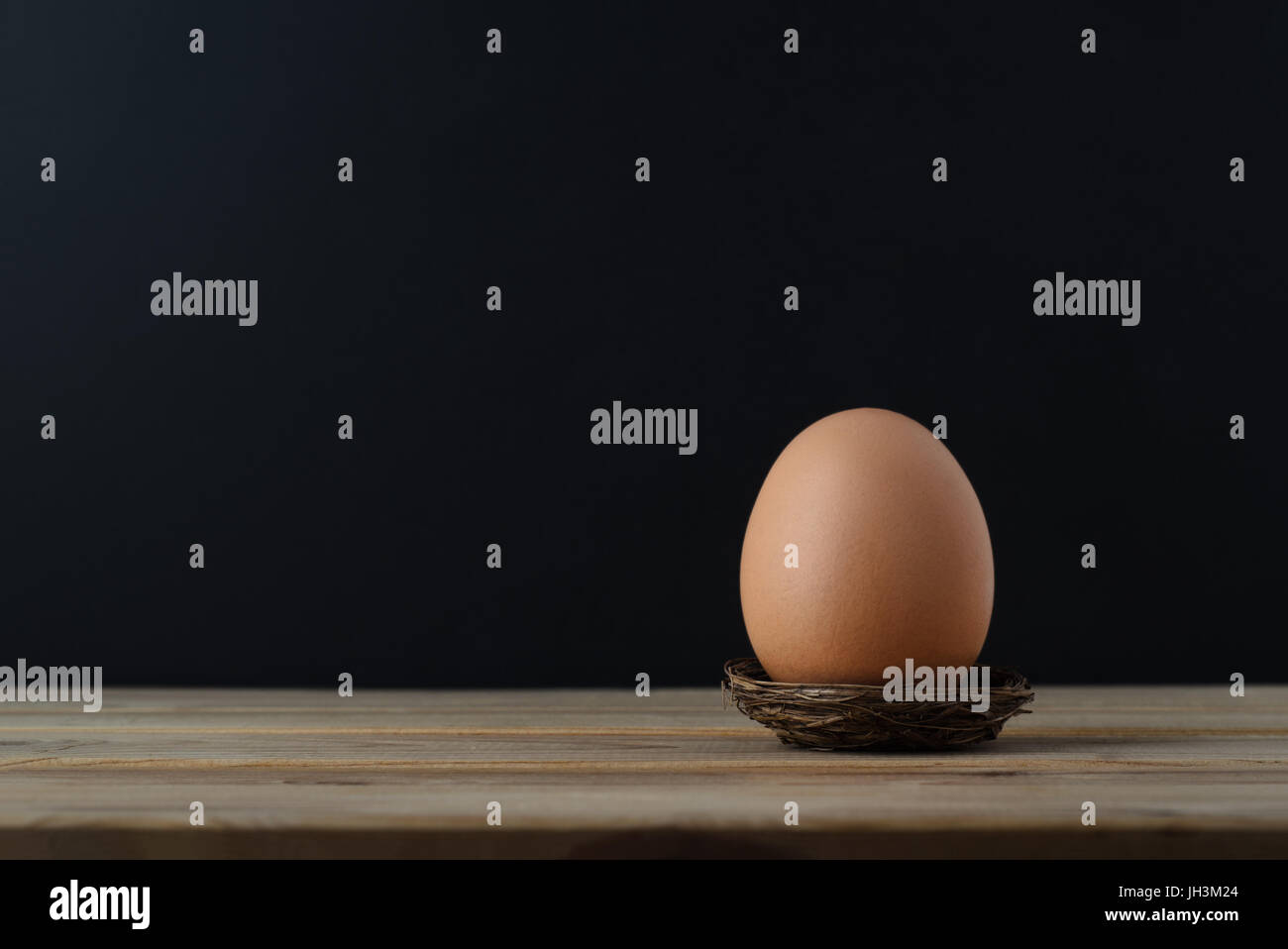 Eine braune Henne-Ei in einem kleinen Nest auf Holzbrett Tisch mit schwarzer Tafel Hintergrund Kopie Raum bieten. Stockfoto