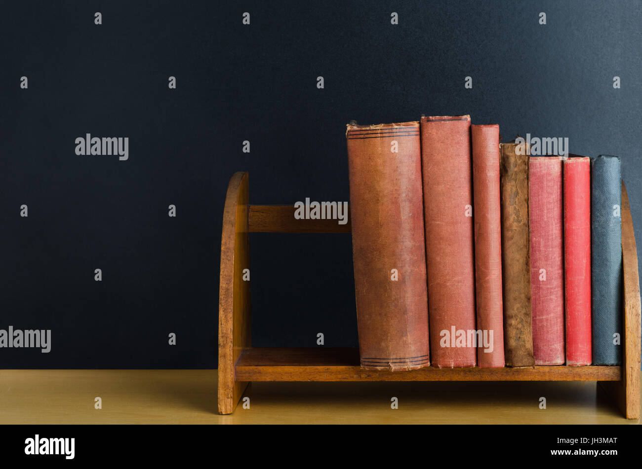 Eine Reihe gebrauchte von alten Bücher mit leeren Buchrücken, aufrecht auf einem Desktop-Regal mit schwarzen Tafel Hintergrund. Stockfoto