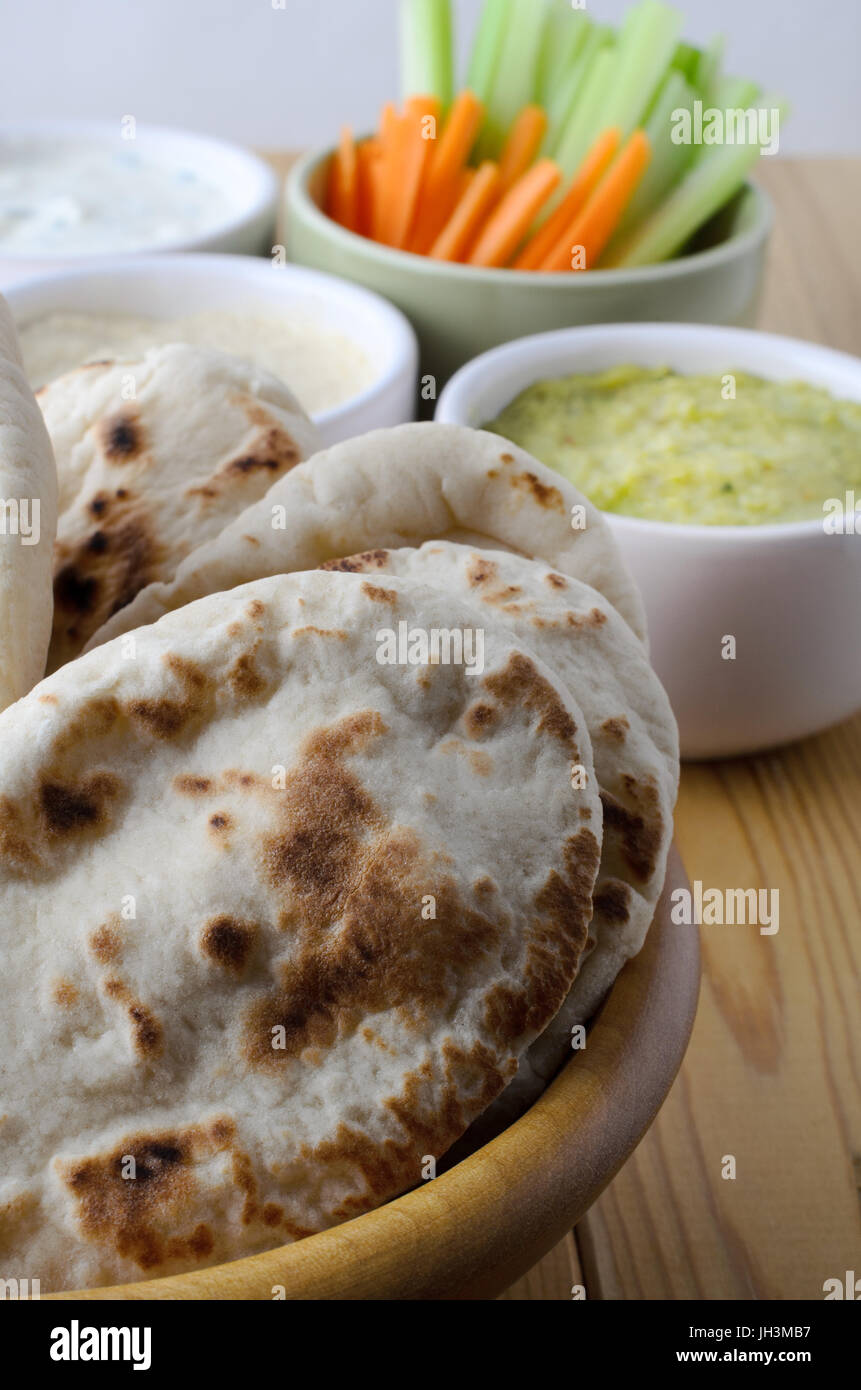 Tisch gedeckt mit einem frische vegetarische Buffet mit Pitta-Brot im Vordergrund und eine Auswahl an Dips mit Crudites in Schälchen im Hintergrund. Stockfoto