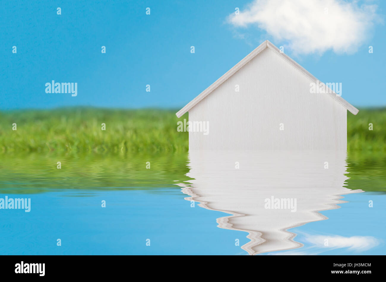 Konzeptionelle Fotografie von einem weißen Holzhaus in hellen grünen Graslandschaft mit blauem Himmel, erscheinen eine Flut von Wasser versinken.  Wasser wurde Stockfoto